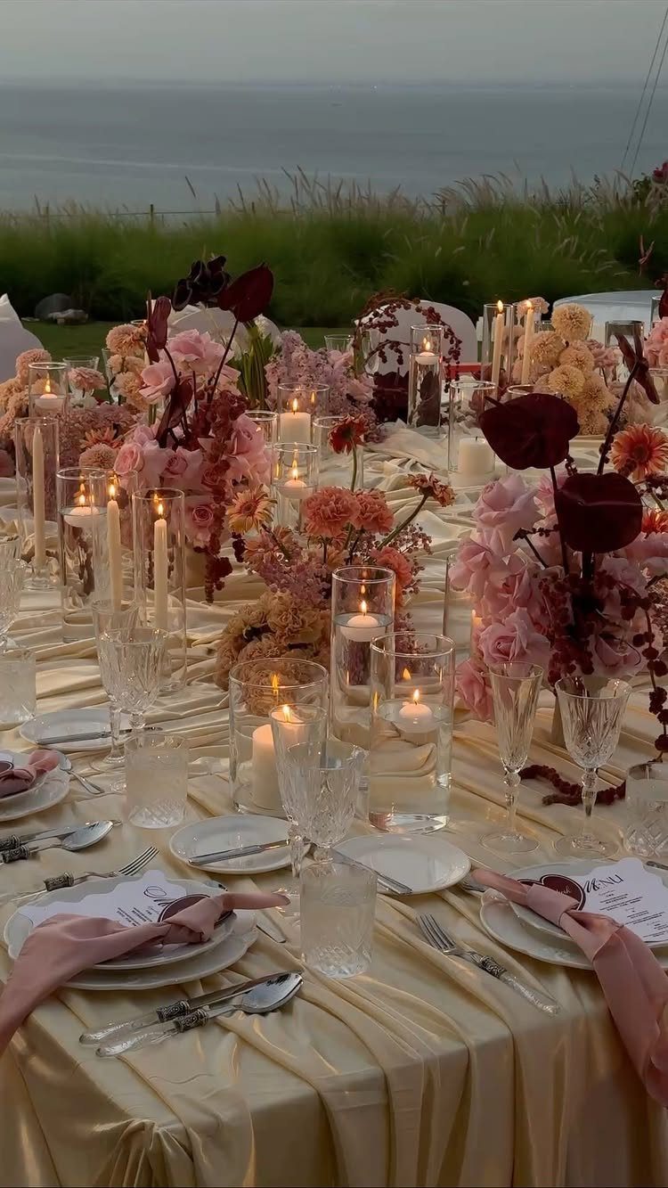 A decorated wedding reception table with pink flowers and glowing candles overlooking the ocean.