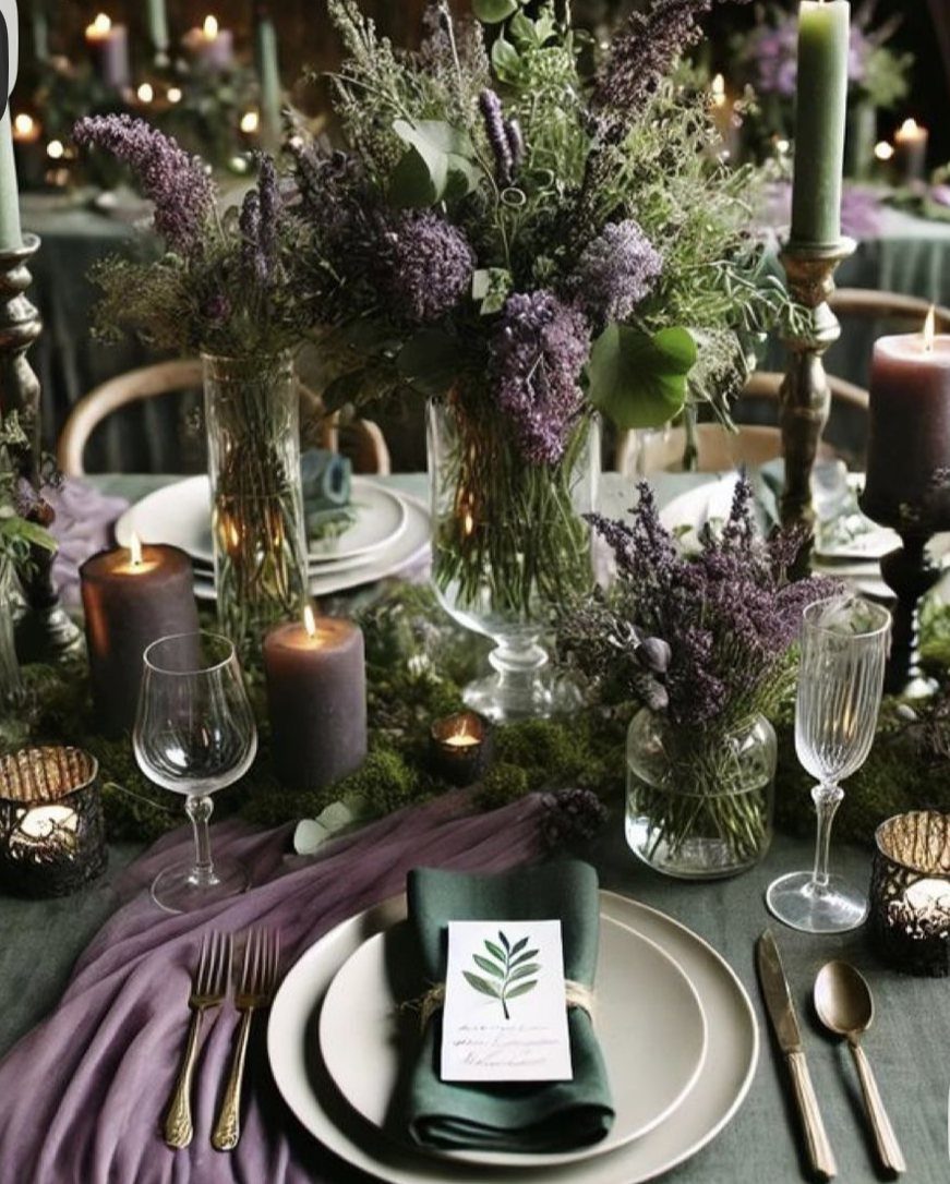 Lavender flowers and green foliage arranged on a wedding table with purple candles and gold cutlery.