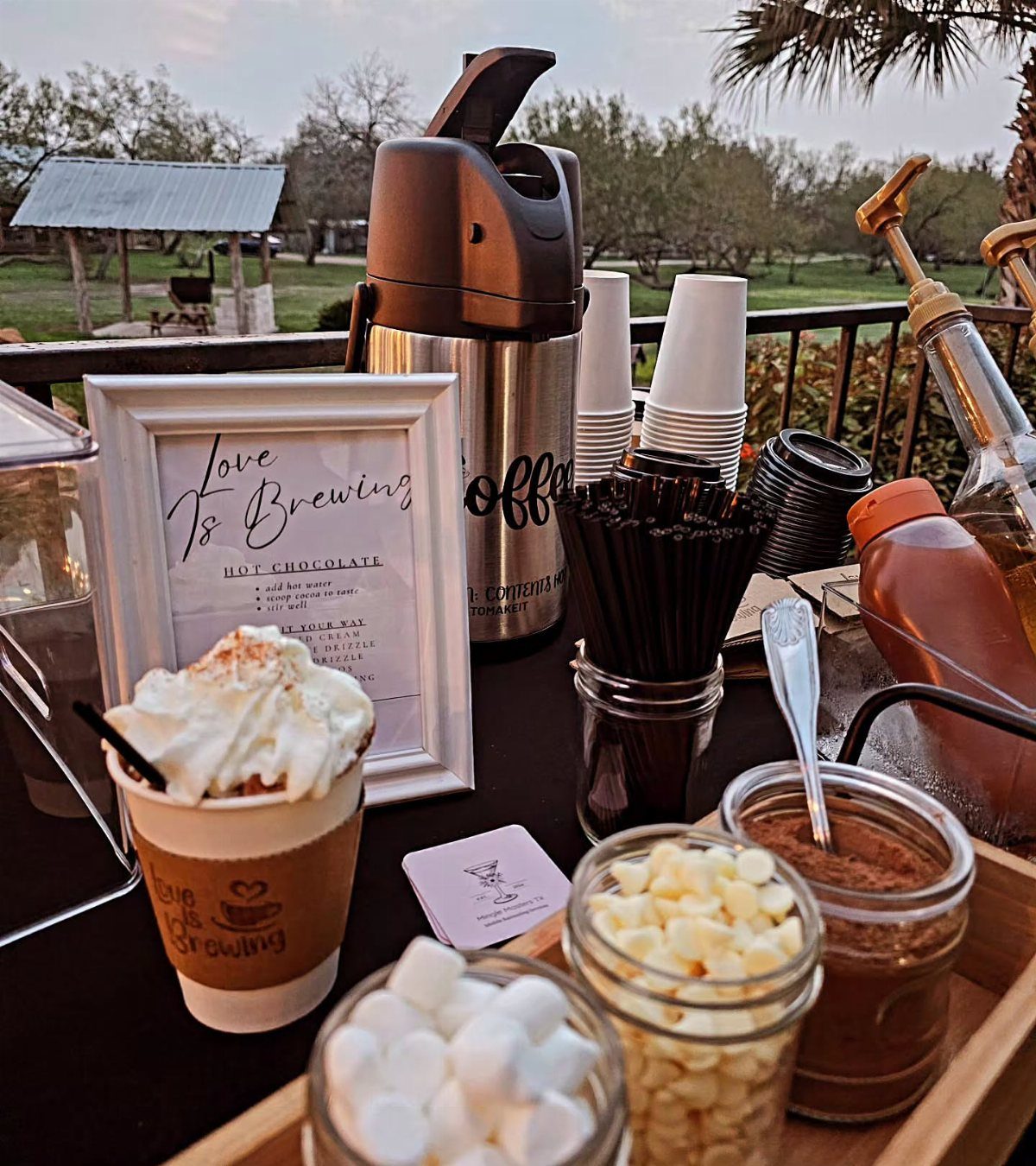 A hot chocolate bar setup with whipped cream, marshmallows, chocolate chips, and a sign saying Love is Brewing.