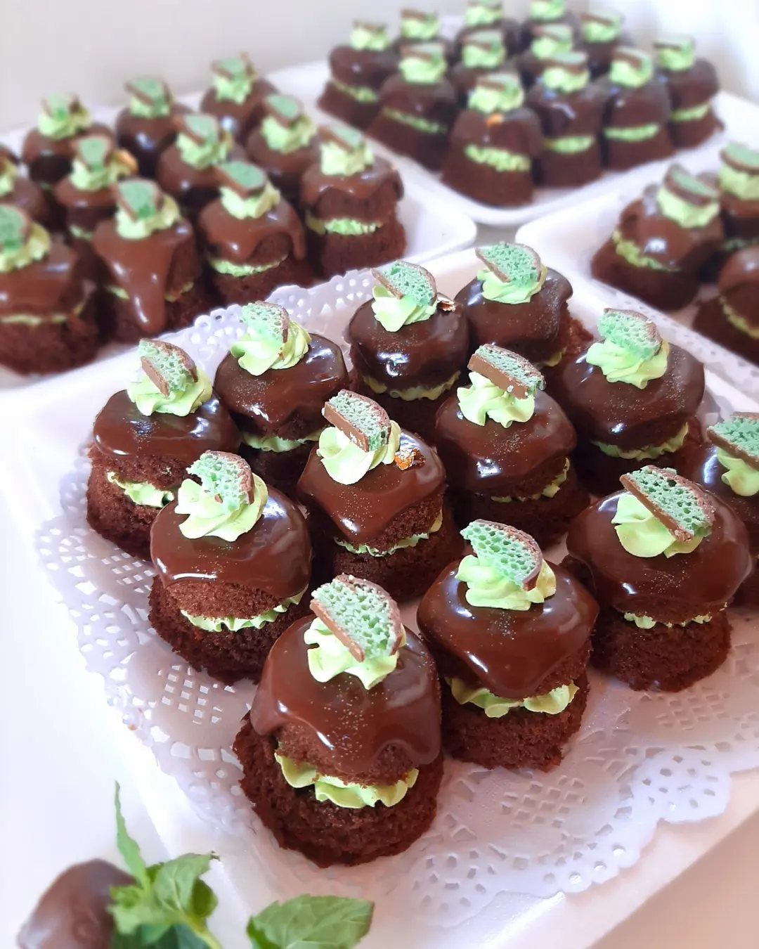 Chocolate cake bites topped with mint frosting and peppermint candy on white platters.