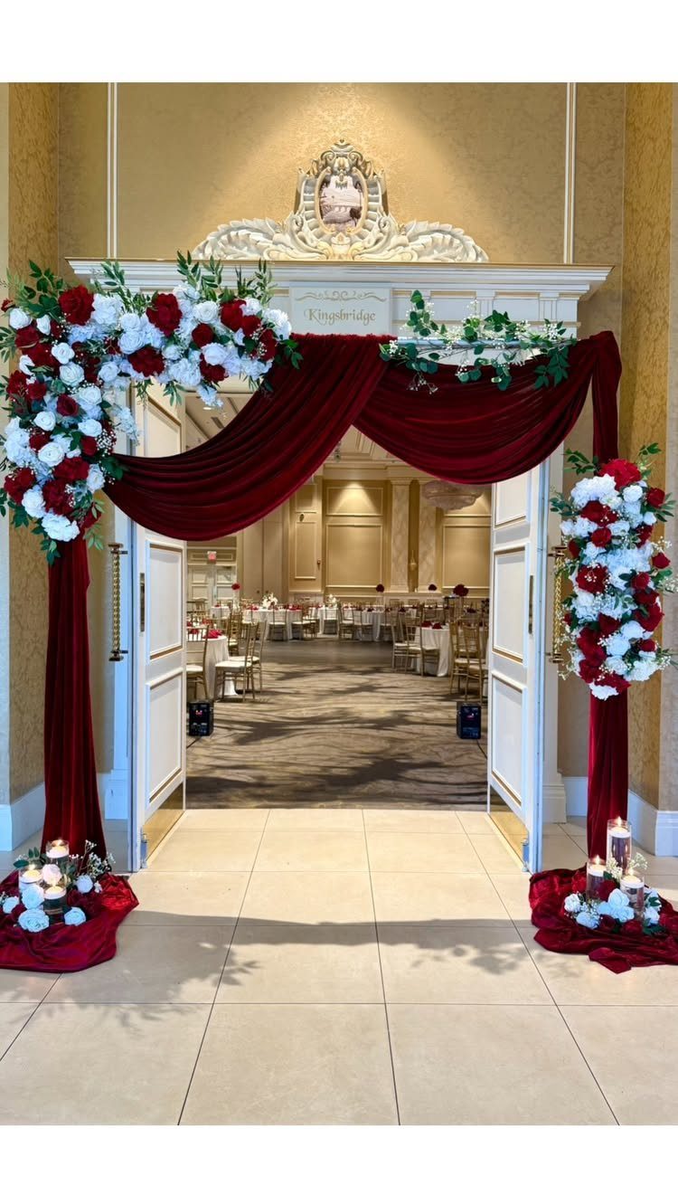 Red velvet fabric and white and red rose arrangements draped over a white doorway entrance.