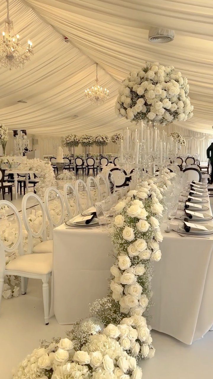 White rose garlands and crystal centerpieces decorate a long wedding reception table under a draped marquee.