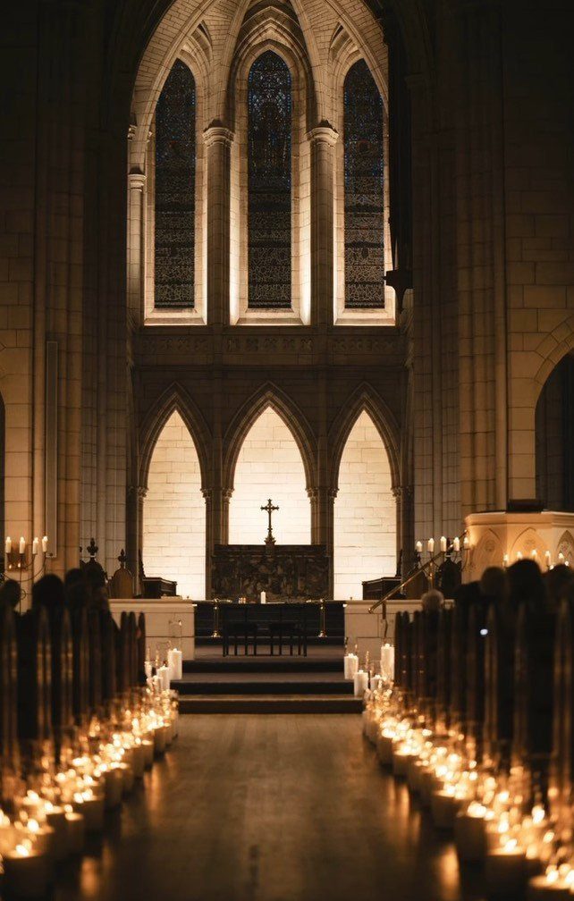 Lit candles line a dark cathedral aisle leading toward a stone altar and cross.