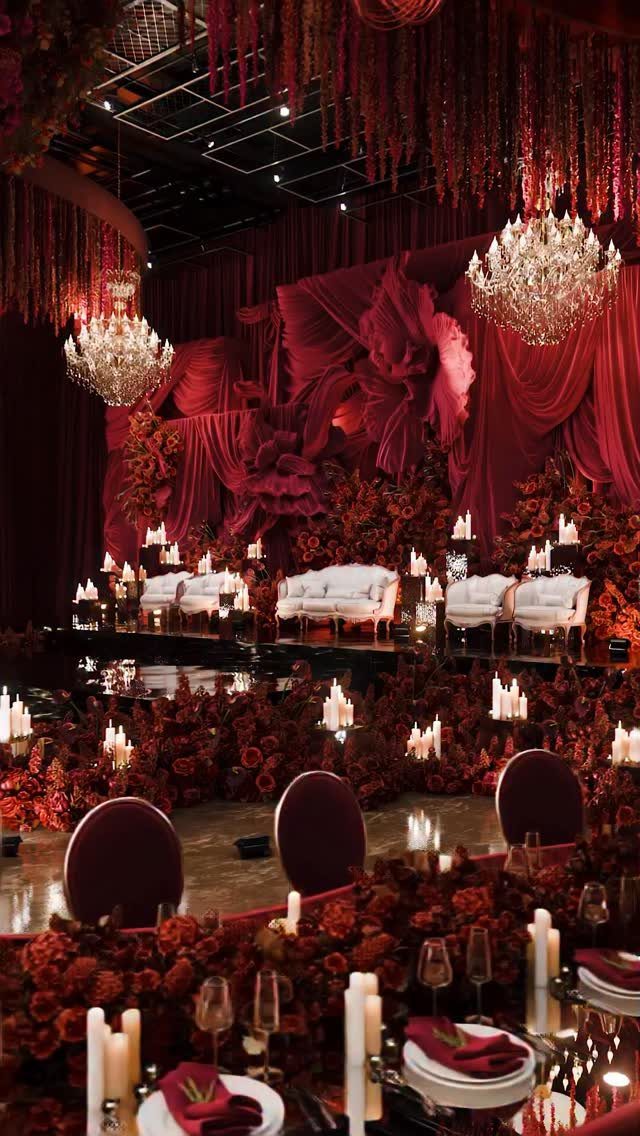 A romantic wedding reception hall decorated with red flowers, white sofas, and glowing candles.