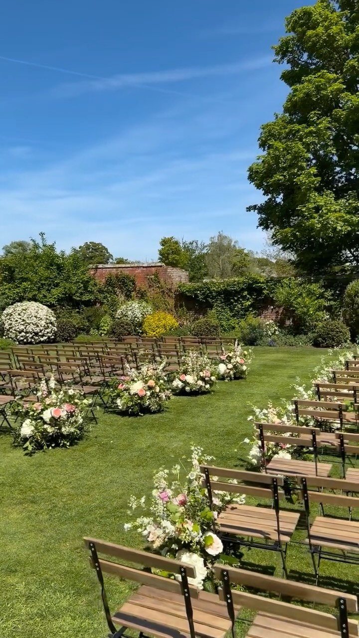 Wooden chairs and floral arrangements arranged on a green lawn for an outdoor wedding ceremony.