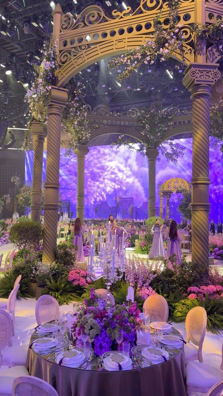 Ornate classical columns and purple floral arrangements decorate a grand, fairytale-themed wedding reception hall.