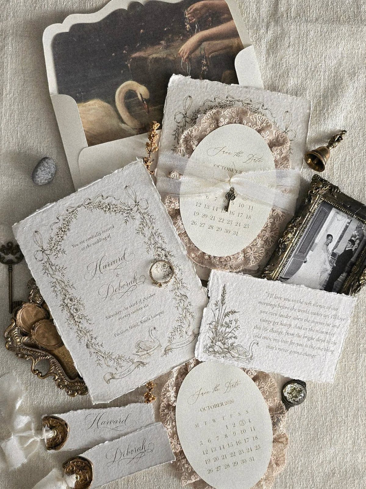 Vintage wedding stationery with calligraphy and lace ruffles scattered on a white textured fabric surface.