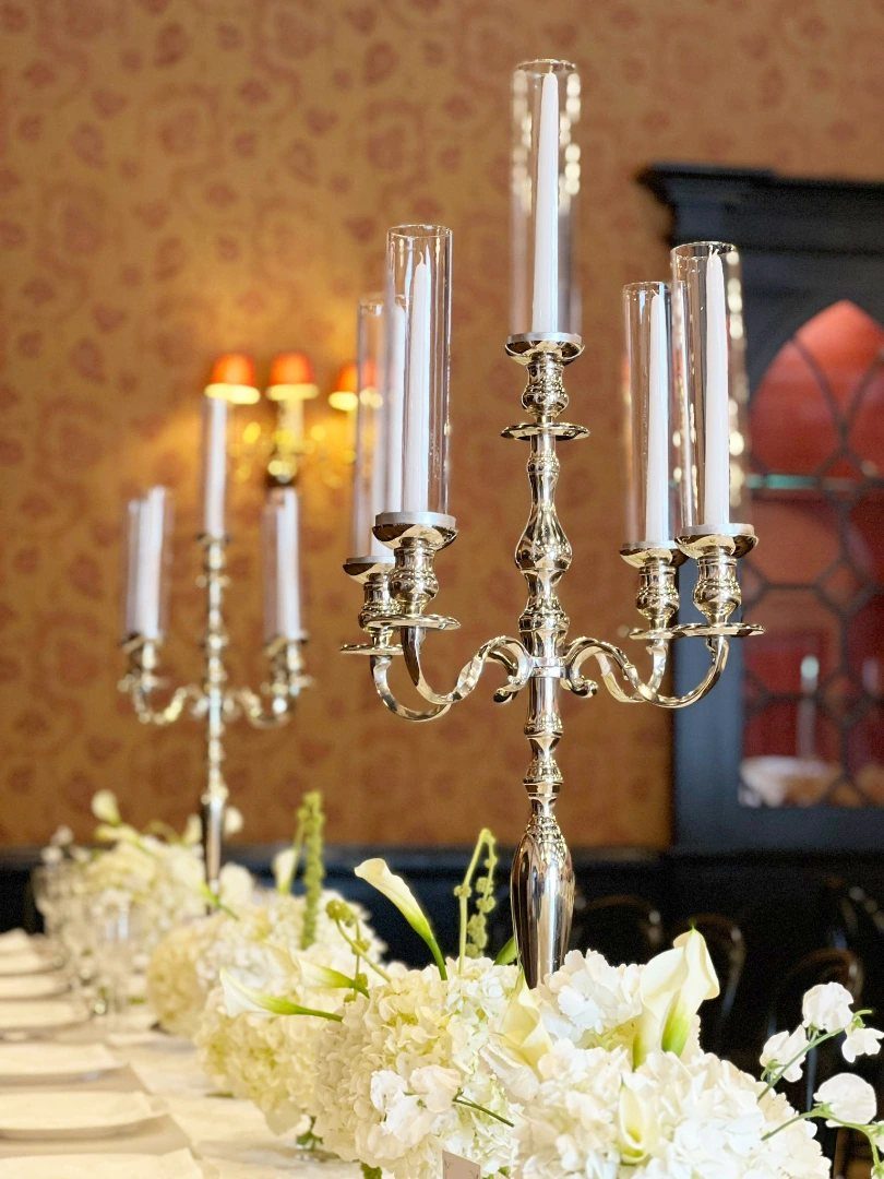 Silver ornate candelabras with white candles arranged among white floral centerpieces on a dining table.