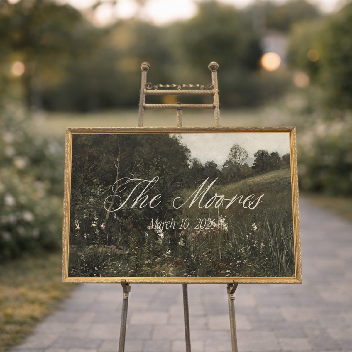 A gold framed wedding welcome sign with calligraphy text on a metal easel outdoors.