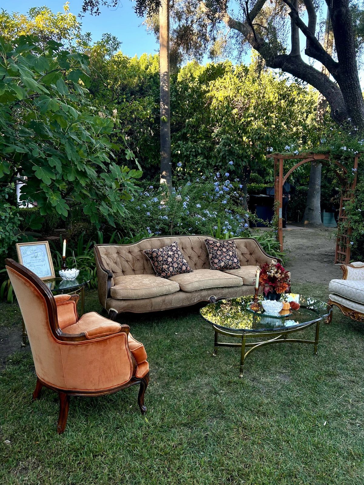 Vintage tufted sofa, velvet armchair, and glass coffee table arranged on a green garden lawn.