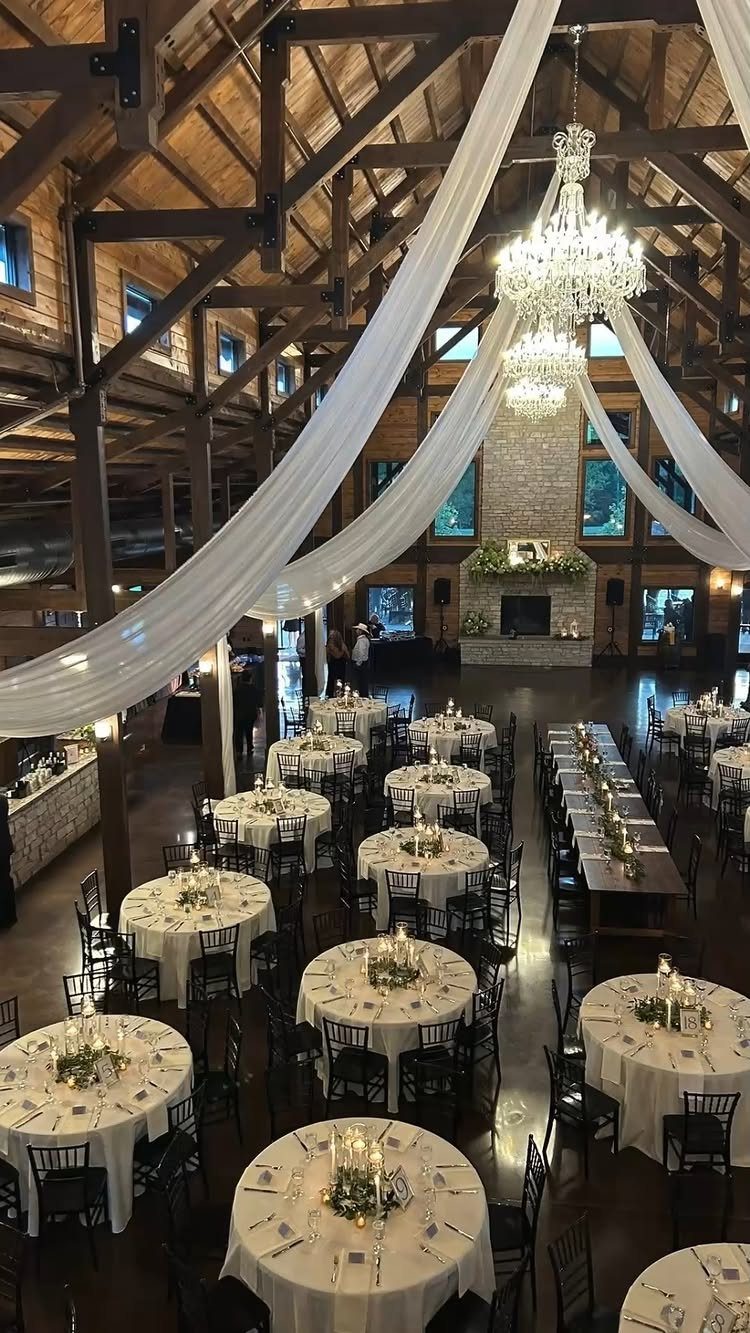A rustic wedding reception hall with wooden beams, white draping, and elegant table settings.