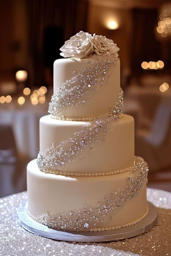 Three-tier white wedding cake decorated with cascading silver crystals and large white sugar roses.