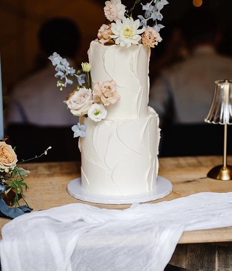 A two-tier white textured buttercream cake decorated with fresh roses and small blue flowers.