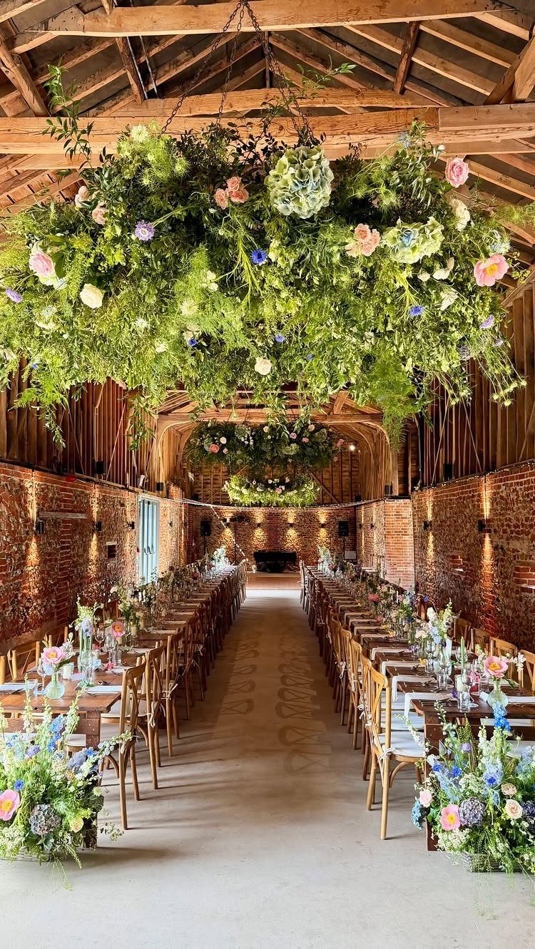 Floral chandeliers hanging over long wooden dining tables in a rustic brick barn wedding reception setting.