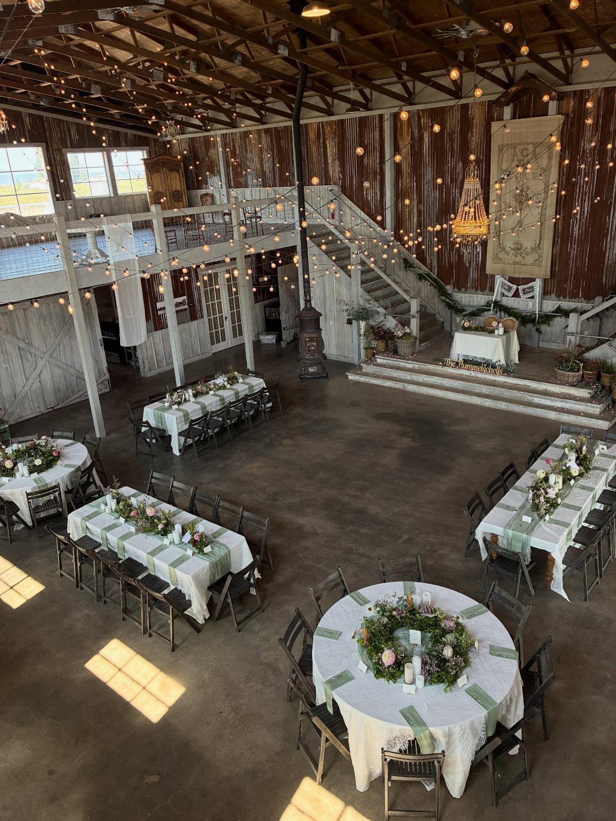 A rustic barn interior decorated with wedding tables, floral centerpieces, and hanging string lights.