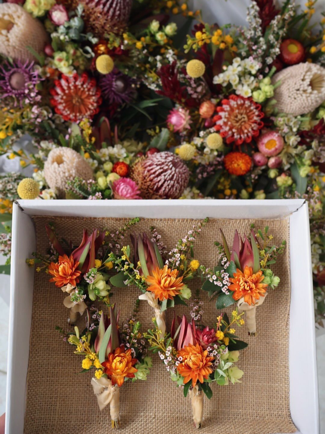 Small floral boutonnieres with orange blossoms and greenery resting in a white box.