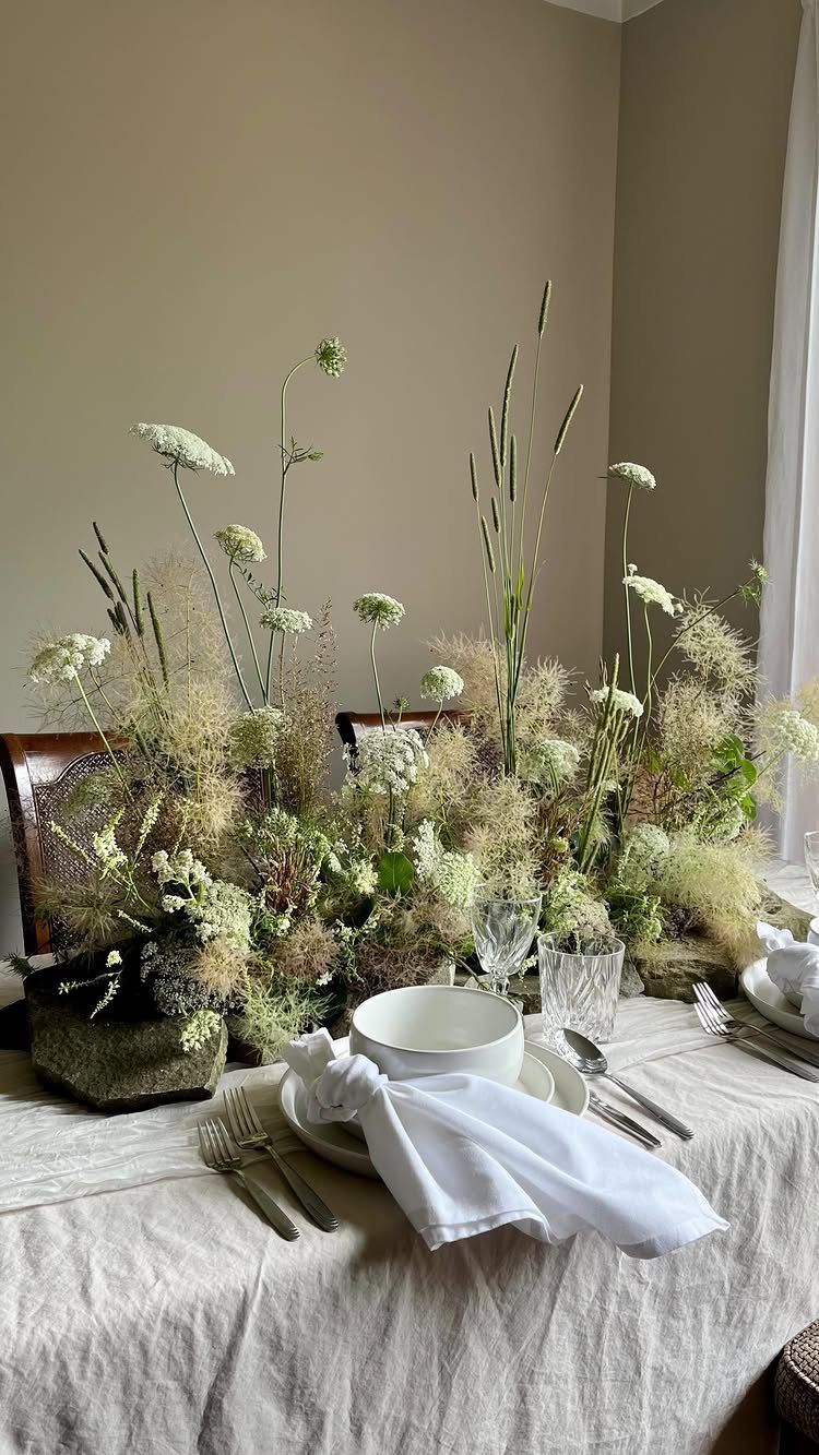 Wildflower arrangement with white blossoms and tall grasses on a linen tablecloth.