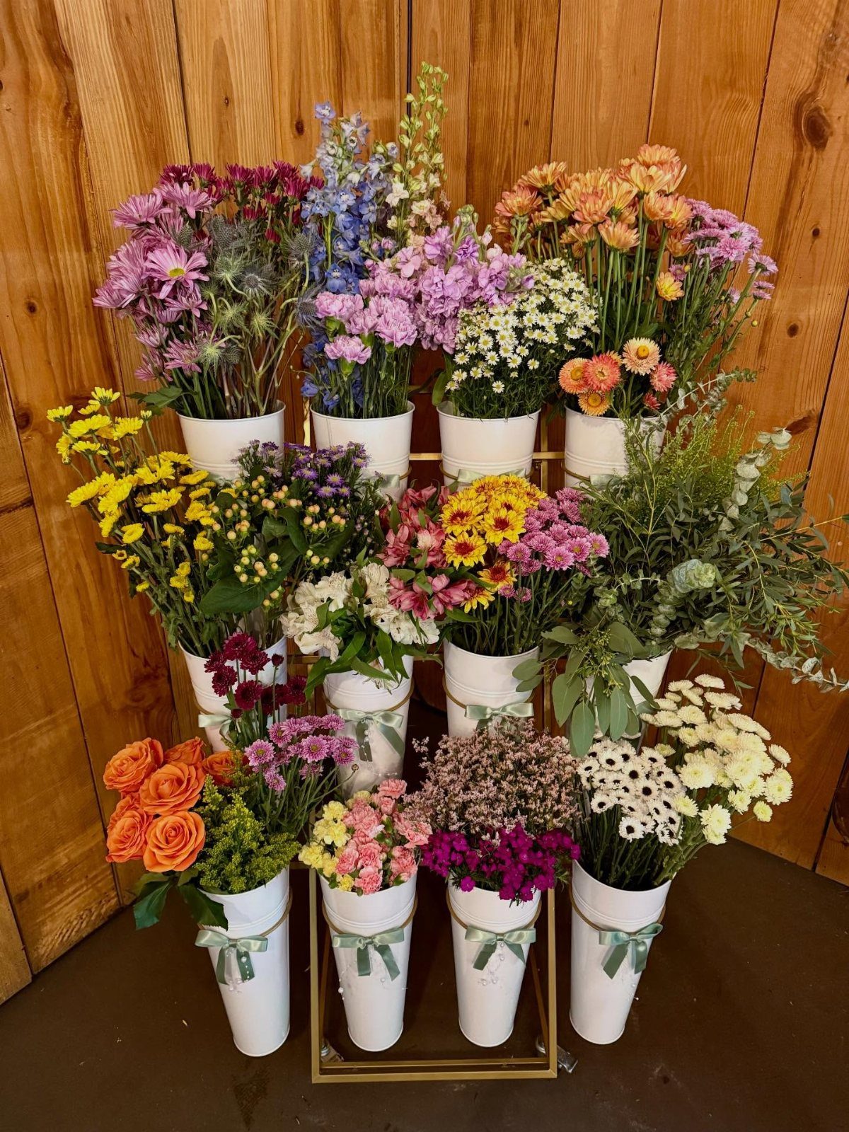 Colorful wildflowers in white buckets arranged on a gold stand against a wooden background.