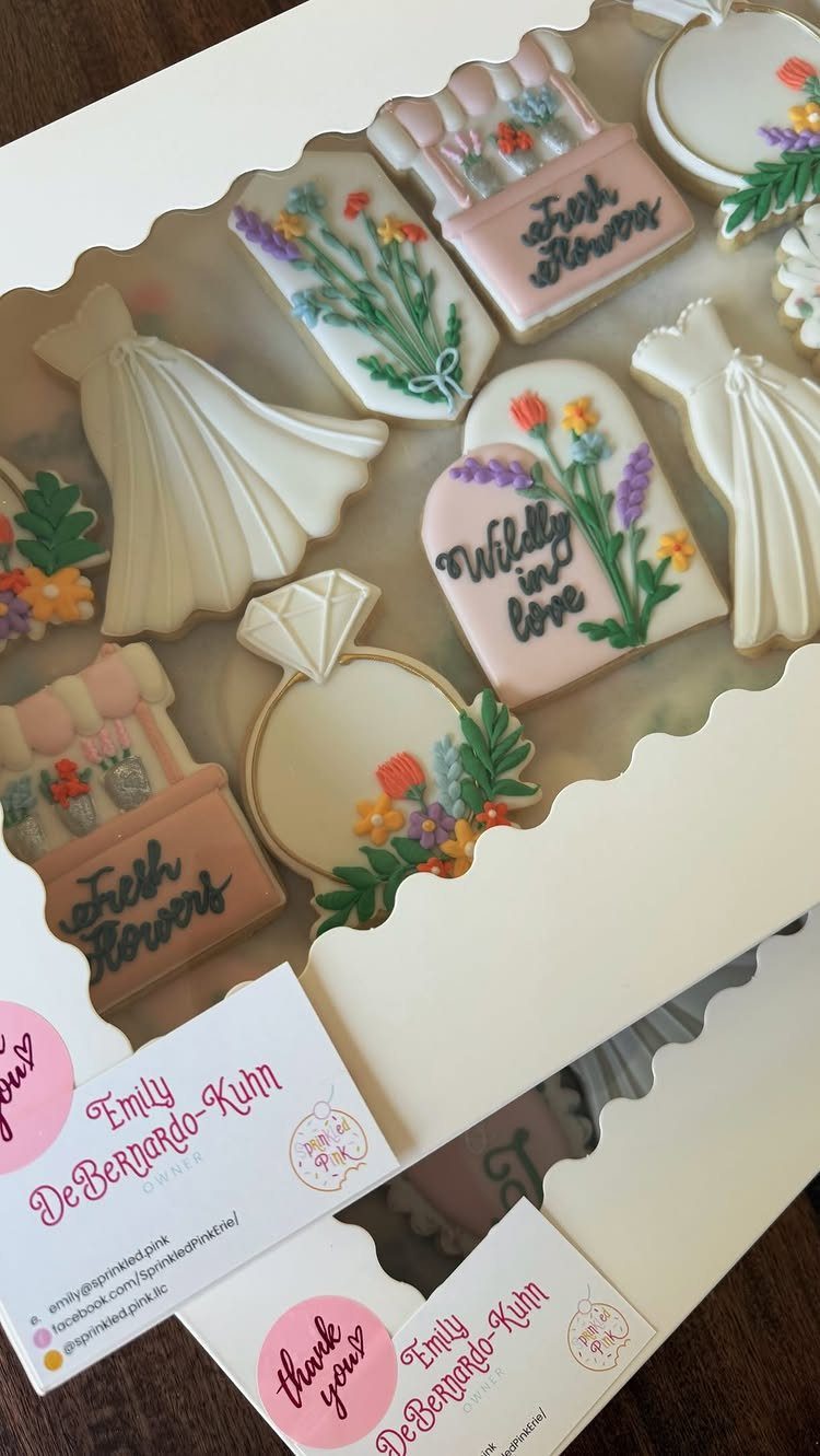 Decorated sugar cookies with wildflower designs and wedding motifs inside a white box.