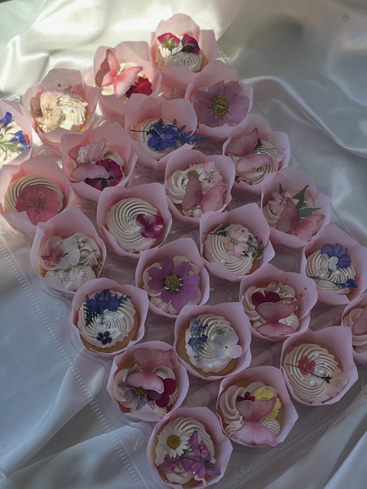 Cupcakes decorated with colorful edible wildflowers arranged on a white draped fabric surface.